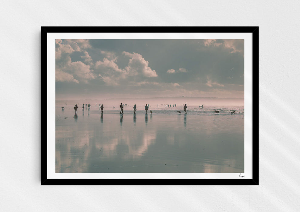 Beach Fever, a colour photographic print  in a black frame depicting the sky and people reflected on Saunton Sands.