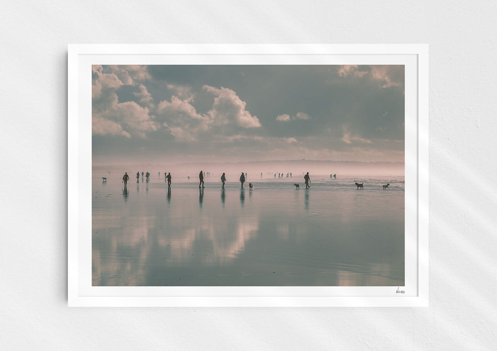 Beach Fever, a colour photographic print  in a white frame depicting the sky and people reflected on Saunton Sands.