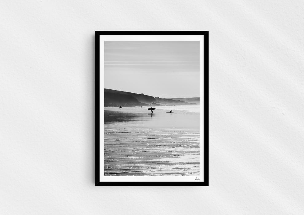 Clear To Land, a black-and-white photo print of surfers on the beach at Polzeath, Cornwall in a black frame.
