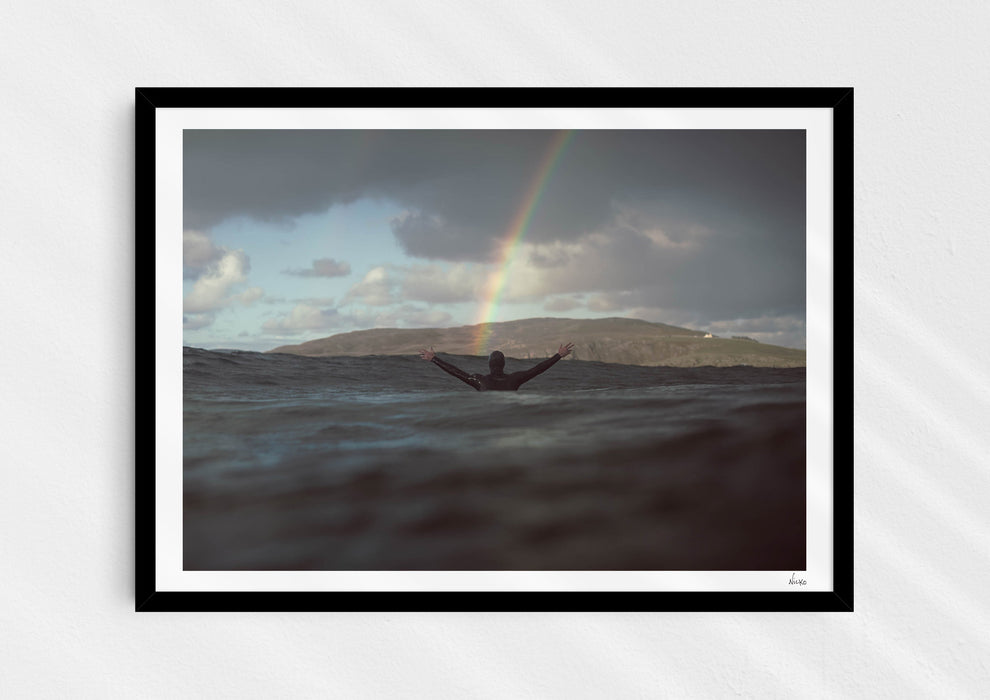 Colours With Colour, a colour photographic print of a surfer saluting a rainbow in Scotland in a black frame.