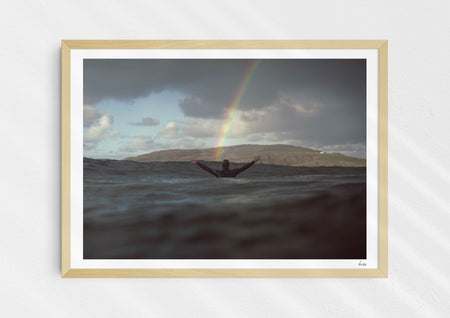 Colours With Colour, a colour photographic print of a surfer saluting a rainbow in Scotland in a wood frame.