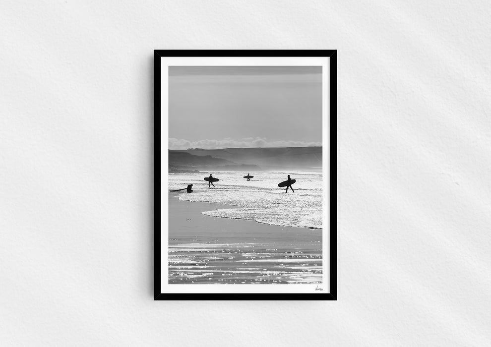 Entry Exits, a black-and-white photo print of surfers on the beach Polzeath, Cornwall in a black frame.
