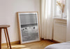 Entry Exits, a black-and-white photo print of surfers on the beach Polzeath, Cornwall in a frame leaning against a wall.