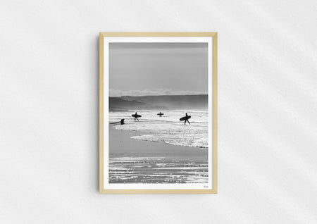 Entry Exits, a black-and-white photo print of surfers on the beach Polzeath, Cornwall in a wood frame.