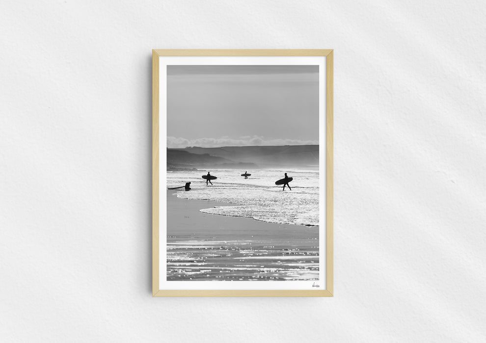 Entry Exits, a black-and-white photo print of surfers on the beach Polzeath, Cornwall in a wood frame.