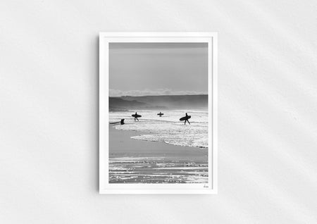 Entry Exits, a black-and-white photo print of surfers on the beach Polzeath, Cornwall in a white frame.
