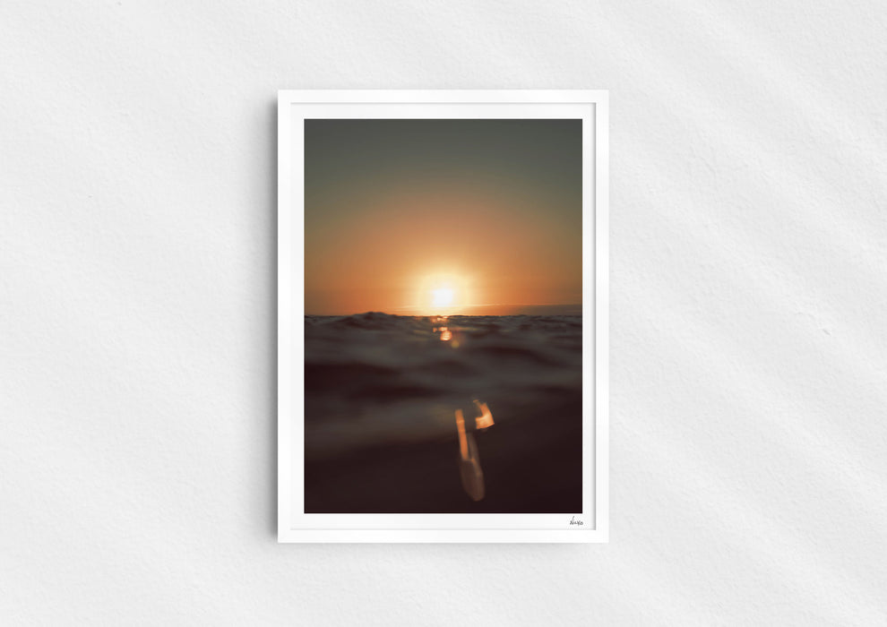 Gold Stripe, a colour photographic print of the sun at the ocean horizon at Croyde Bay, Devon in a white frame.