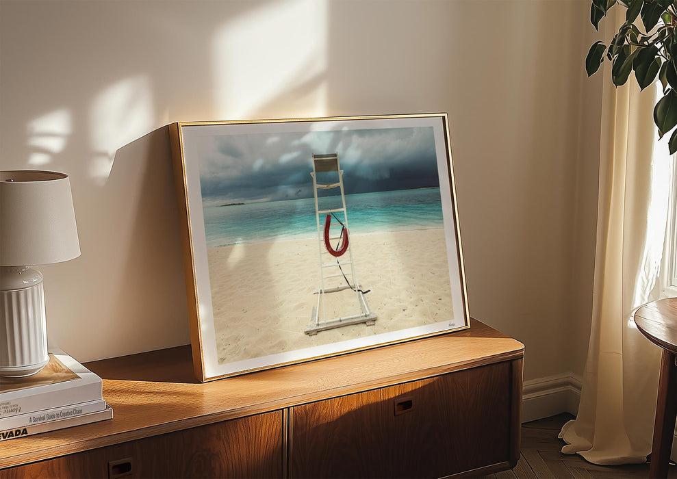 A framed print in a room of Lifeguard Not Included, a colour photograph of a lifeguard chair on a white sandy beach.