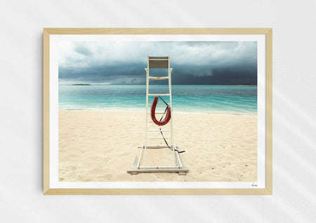 Lifeguard Not Included, a colour photographic print of a lifeguard chair on a white sandy beach. in a wood frame.