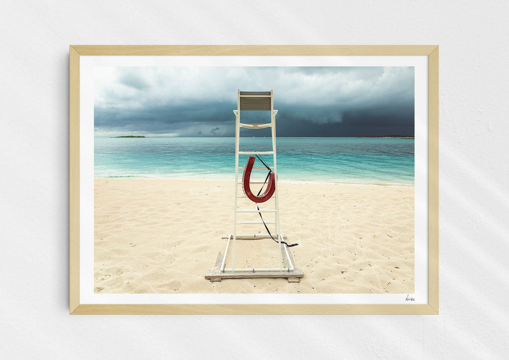 Lifeguard Not Included, a colour photographic print of a lifeguard chair on a white sandy beach. in a wood frame.