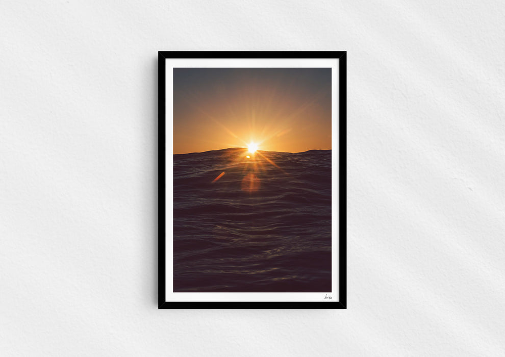 Light in the Deep, a colour photographic print of the sun on the ocean horizon at Porthtowan, Cornwall in a black frame.