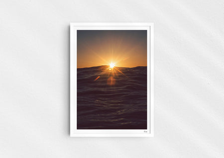 Light in the Deep, a colour photographic print of the sun on the ocean horizon at Porthtowan, Cornwall in a white frame.