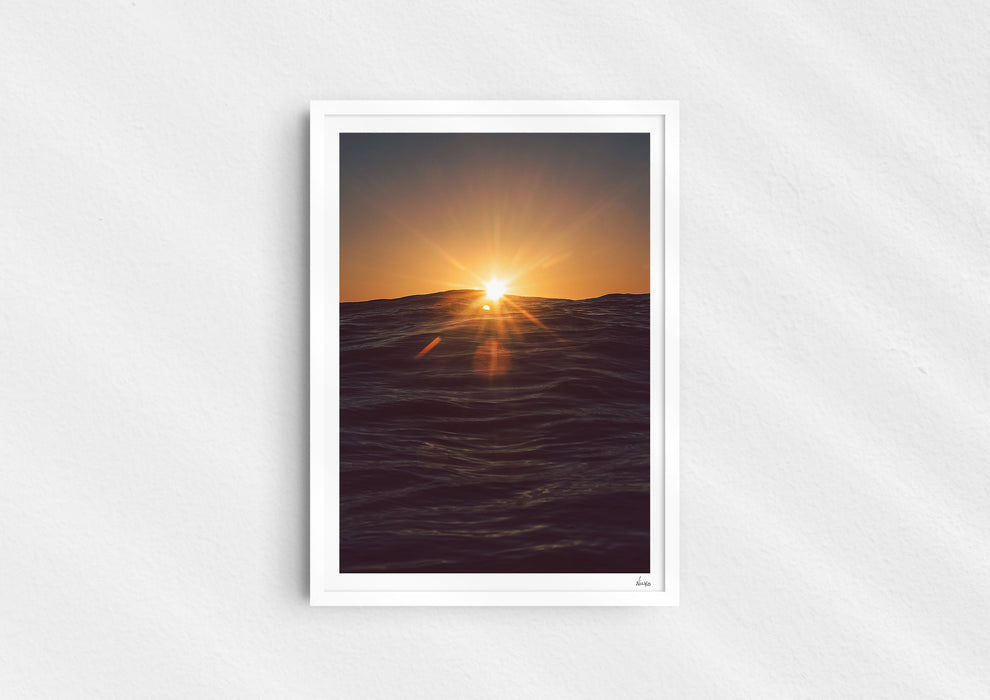 Light in the Deep, a colour photographic print of the sun on the ocean horizon at Porthtowan, Cornwall in a white frame.