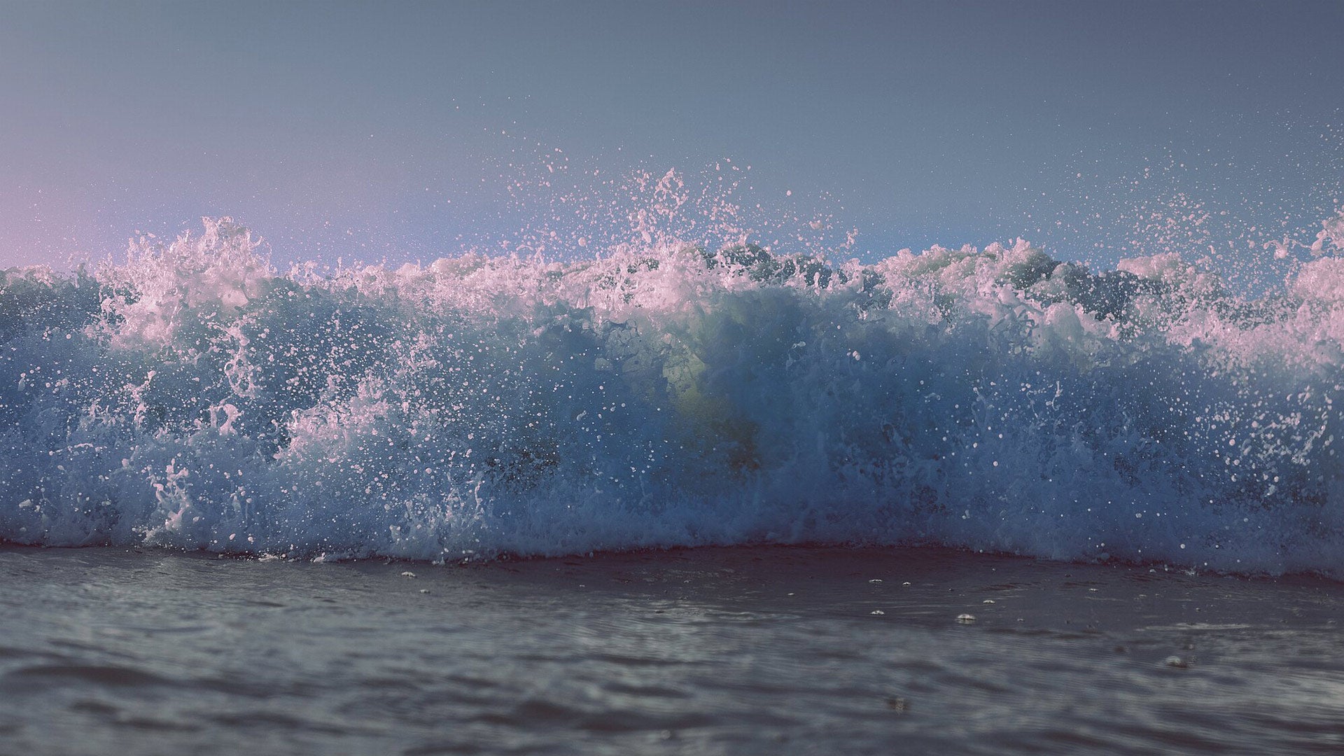 Powerful wave crashing against the shore with a clear blue sky.