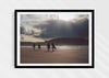 Mutual People, a colour photographic print of surfers walking across sand in northern Scotland in a black frame.