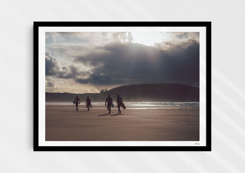 Mutual People, a colour photographic print of surfers walking across sand in northern Scotland in a black frame.