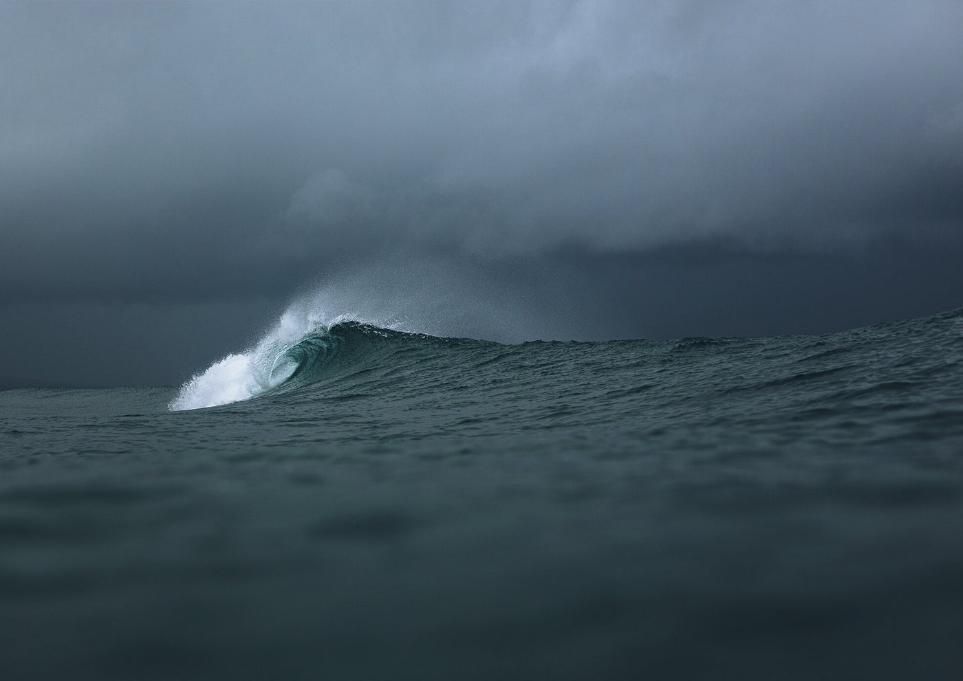 Large wave crashing in the ocean under a dark, stormy sky