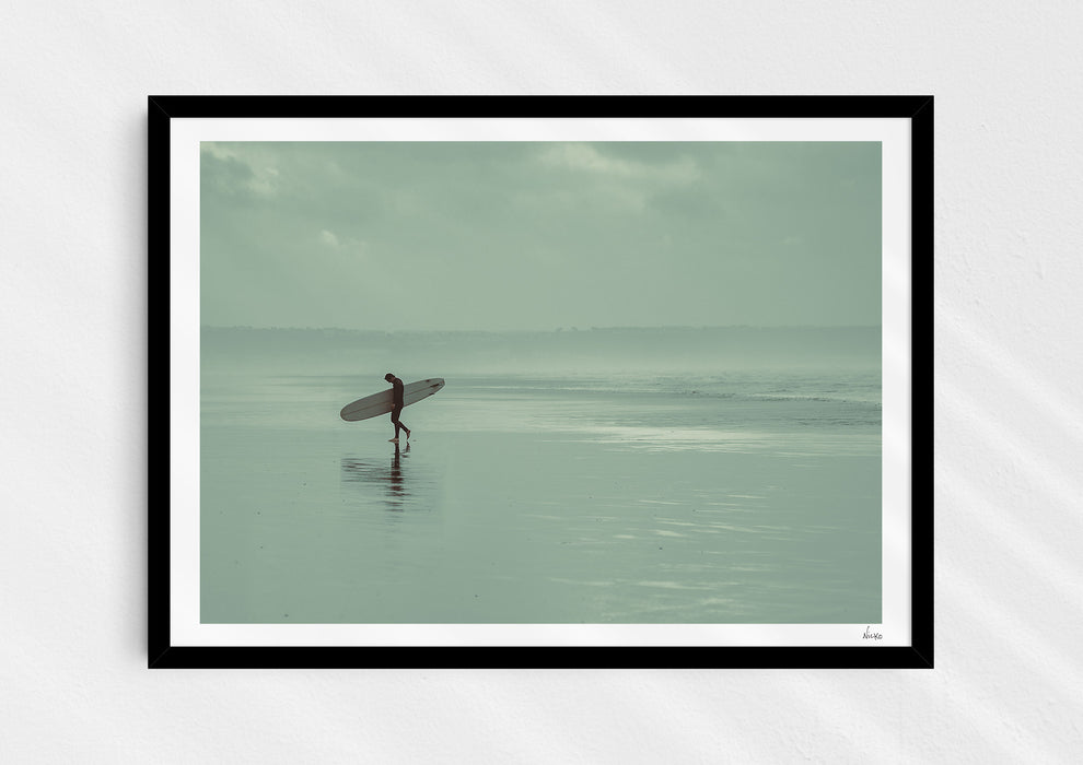 Sea Wanderer, a colour photographic print of a surfer walking across Saunton Sands, Devon in a black frame.