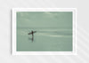 Sea Wanderer, a colour photographic print of a surfer walking across Saunton Sands, Devon in a white frame.