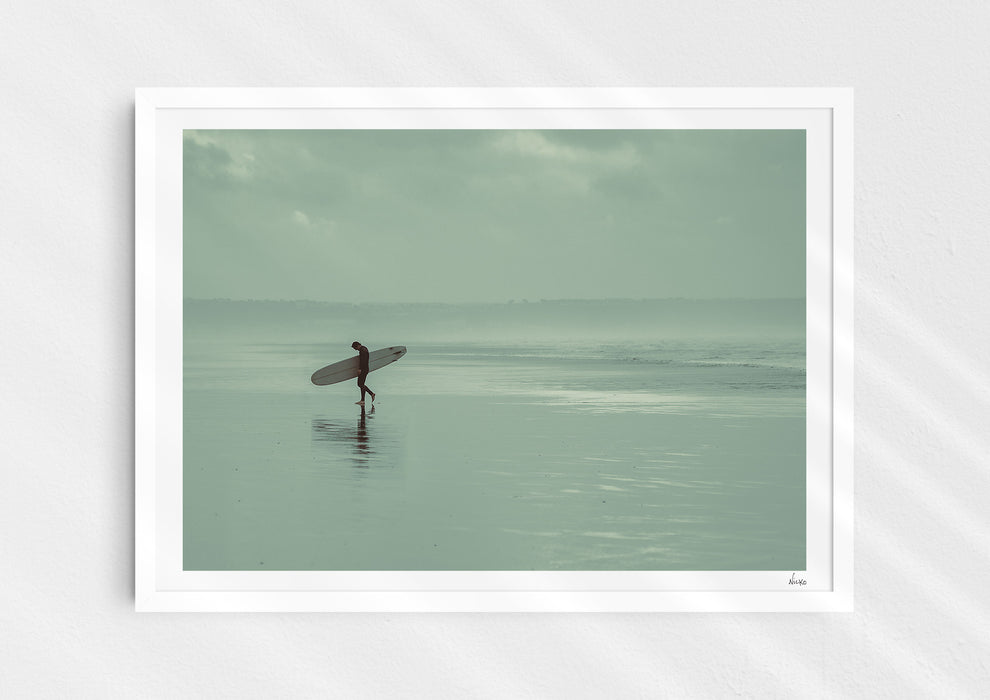 Sea Wanderer, a colour photographic print of a surfer walking across Saunton Sands, Devon in a white frame.
