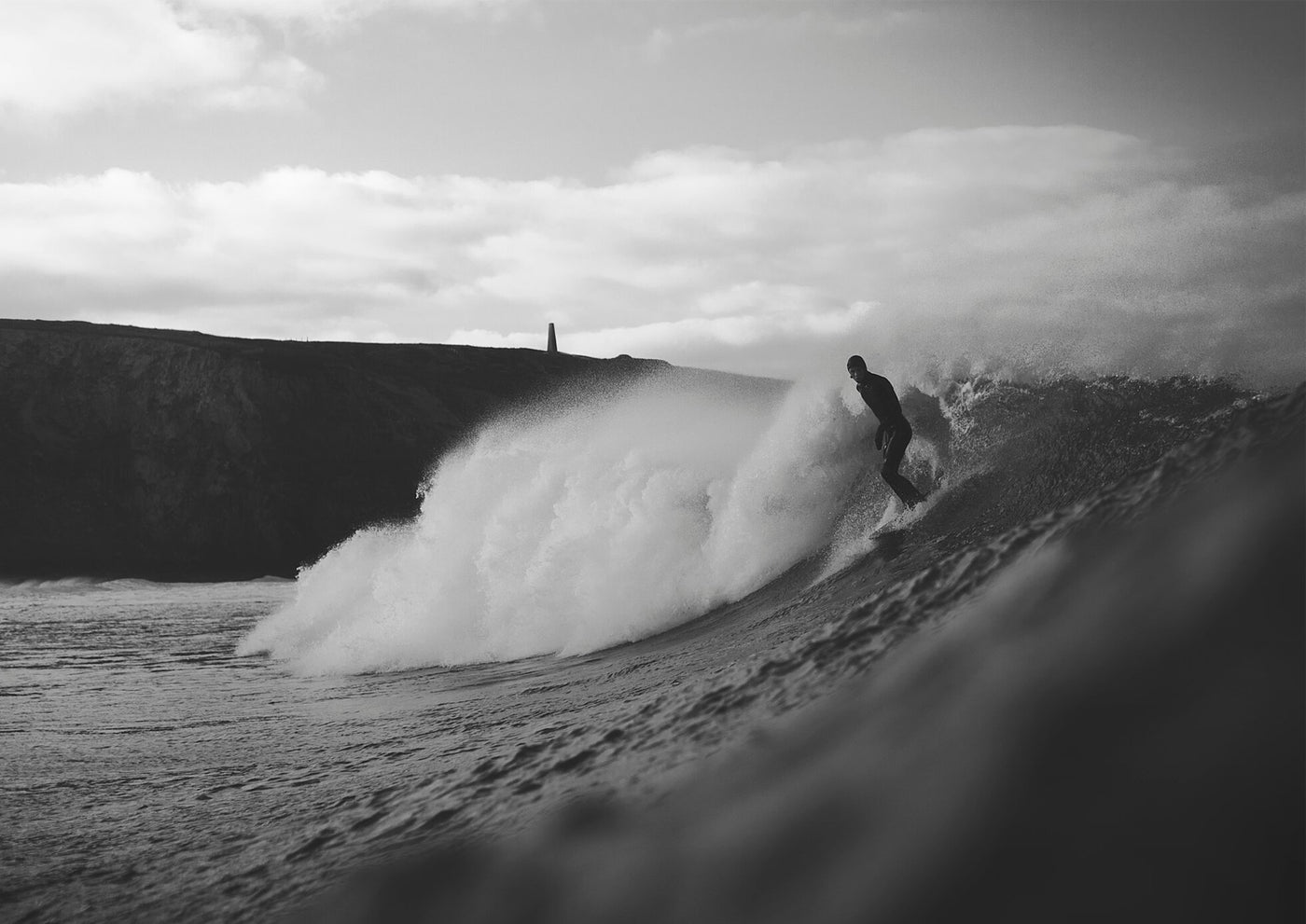 Black and white photo of a surfer riding a large wave in Cornwall.