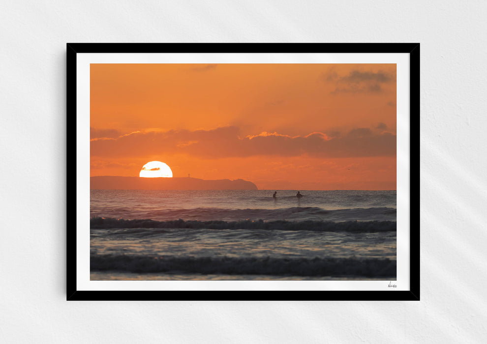 Watching Her Sink, a colour photographic print of surfers at sunset at Croyde Bay, Devon in a black frame.