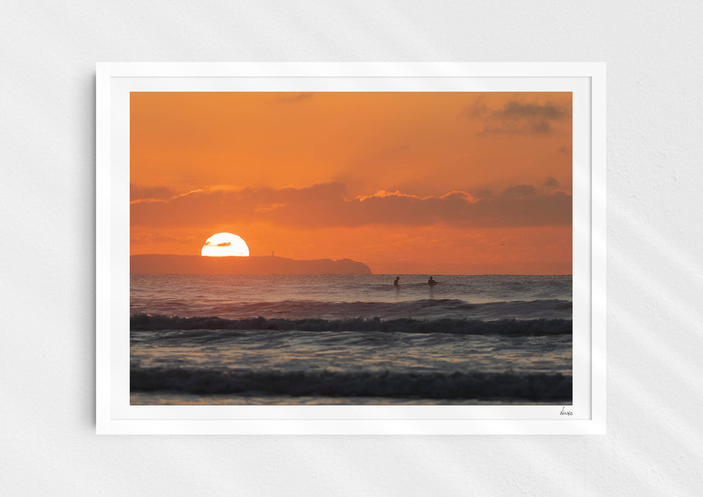 Watching Her Sink, a colour photographic print of surfers at sunset at Croyde Bay, Devon in a white frame.