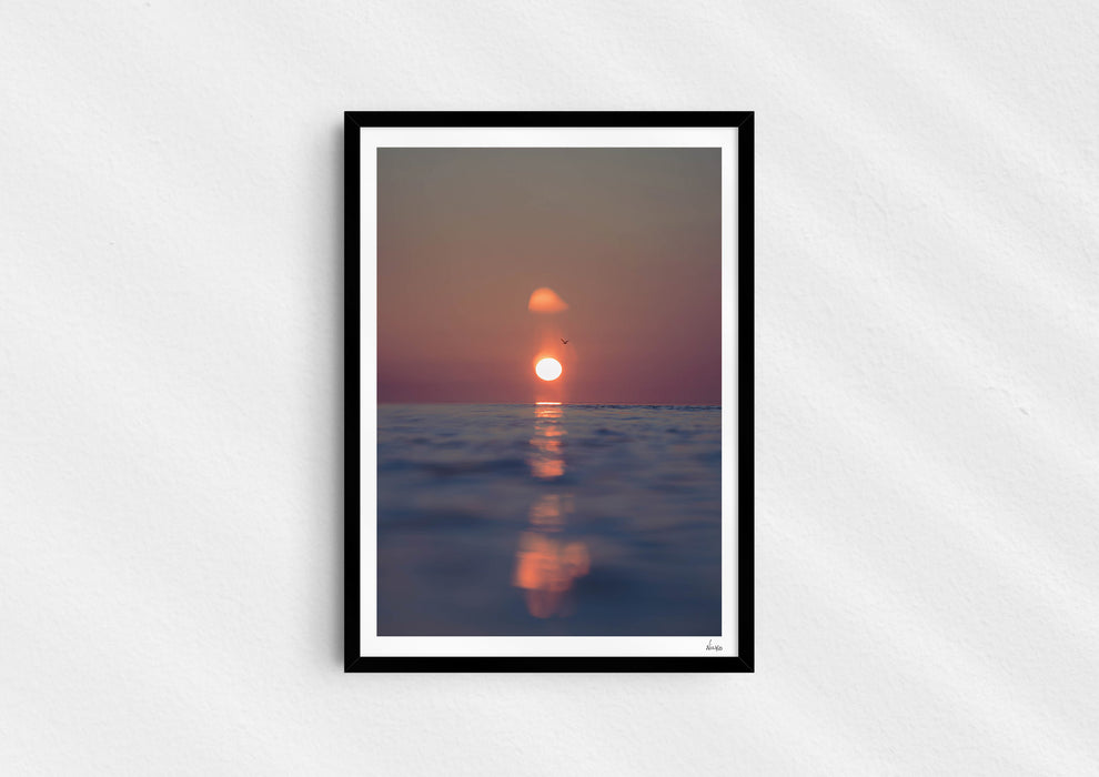 We’ll Meet Again, a colour photographic print of a bird and sunset over a calm ocean in a black frame.