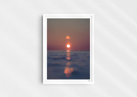 We’ll Meet Again, a colour photographic print of a bird and sunset over a calm ocean in a white frame.