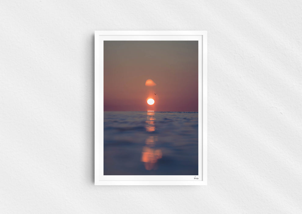 We’ll Meet Again, a colour photographic print of a bird and sunset over a calm ocean in a white frame.